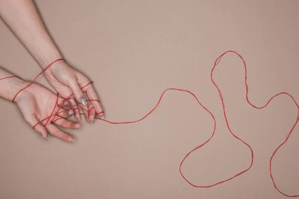 Top view of female hands wrapped in red string on beige background — Stock Photo