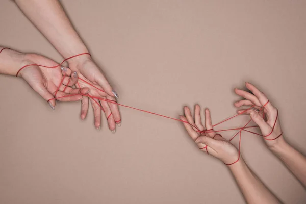 Top view of hands of women wrapped in red thread on beige background — Stock Photo