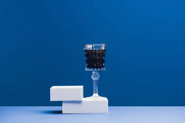 Dark blue beverage in wine glass on cubes on classic blue background — Stock Photo