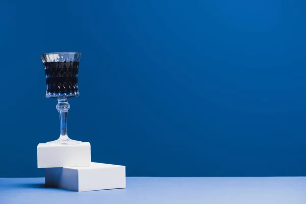 Weinglas mit blauer Flüssigkeit auf Blöcken auf klassisch blauem Hintergrund — Stockfoto
