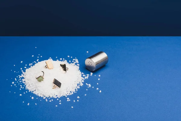 Ювелірні кільця на купі солі з соляним шейкером на класичному синьому фоні — стокове фото