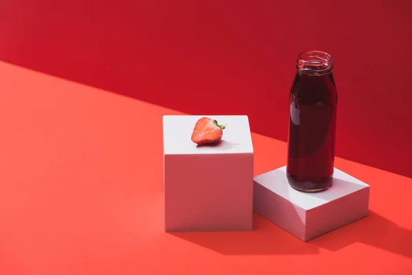 Свіжий ягідний сік у скляній пляшці біля стиглої полуниці на кубиках на червоному тлі — стокове фото