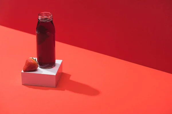 Fresh berry juice in glass bottle near ripe strawberry on cube on red background — Stock Photo