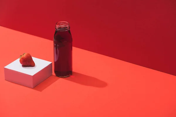 Fresh berry juice in glass bottle near ripe strawberry on cube on red background — Stock Photo