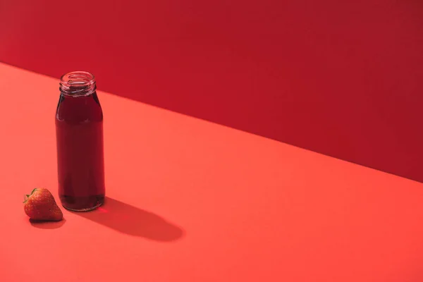 Succo di bacca fresca in bottiglia di vetro vicino alla fragola matura su sfondo rosso — Foto stock