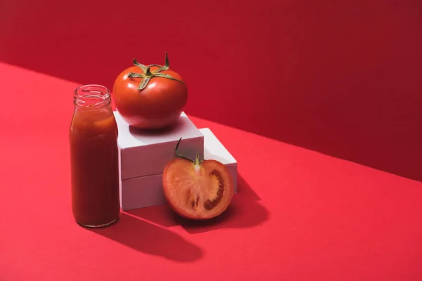 Jugo de verduras frescas en botella de vidrio cerca de tomates maduros en cubos sobre fondo rojo - foto de stock