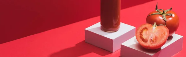 Fresh vegetable juice in glass bottle and ripe tomatoes on cubes on red background, panoramic shot — Stock Photo