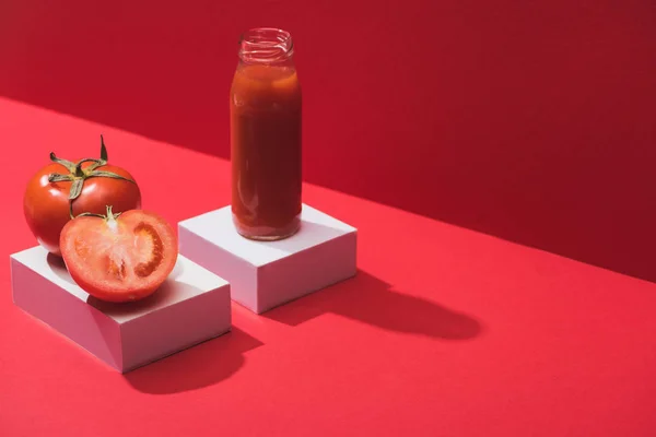 Jugo de verduras frescas en botella de vidrio y tomates maduros en cubos sobre fondo rojo — Stock Photo