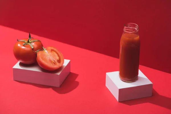 Jugo de verduras frescas en botella de vidrio y tomates maduros en cubos sobre fondo rojo - foto de stock