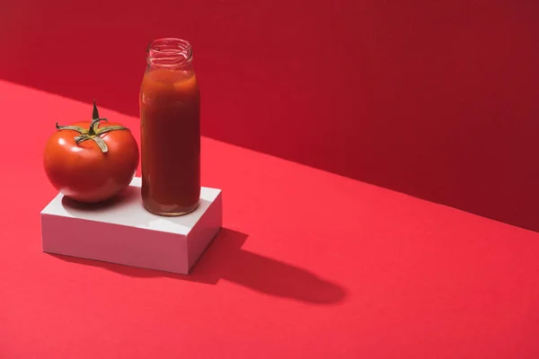 Suco de legumes frescos em garrafa de vidro e tomate maduro no cubo no fundo vermelho — Fotografia de Stock