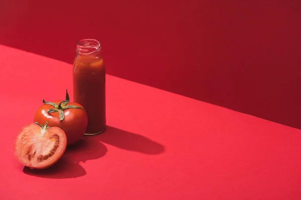 Frischer Gemüsesaft in Glasflasche und reife Tomaten auf rotem Hintergrund — Stockfoto