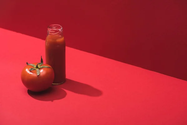 Frischer Gemüsesaft in Glasflasche und reife Tomaten auf rotem Hintergrund — Stockfoto