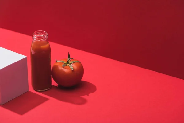 Свежий овощной сок в стеклянной бутылке возле спелых помидоров и куба на красном фоне — стоковое фото