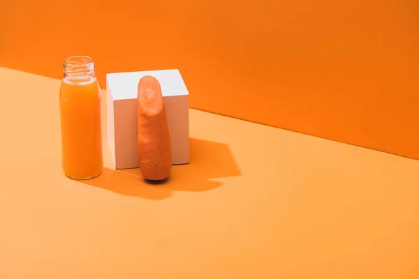 Fresh juice in glass bottle near ripe carrot and cube on orange background — Stock Photo