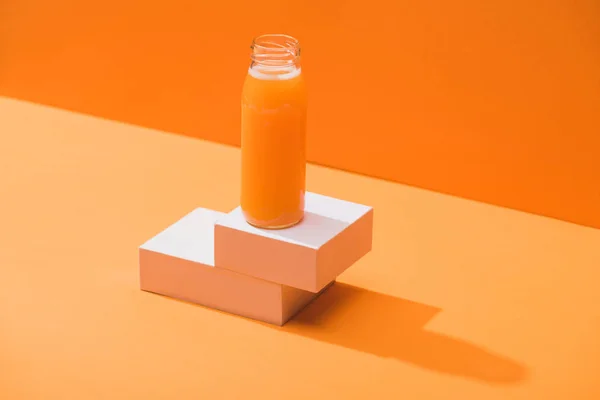 Zumo de zanahoria fresca en botella de vidrio en cubos sobre fondo naranja - foto de stock