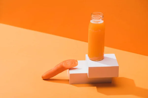 Frischer Saft in Glasflasche nahe reifer Karotte auf Würfeln auf orangefarbenem Hintergrund — Stockfoto