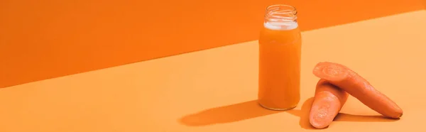 Jus frais en bouteille de verre près de carottes mûres sur fond orange, panoramique — Photo de stock