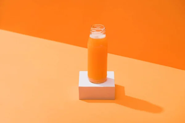 Fresh carrot juice in glass bottle on cube on orange background — Stock Photo