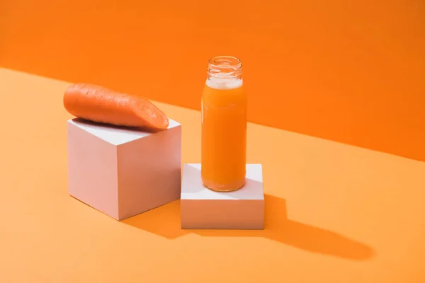 Frischer Saft in Glasflasche nahe reifer Karotte auf Würfeln auf orangefarbenem Hintergrund — Stockfoto