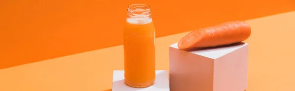 Свежий сок в стеклянной бутылке возле спелой морковки на кубиках на оранжевом фоне, панорамный снимок — стоковое фото