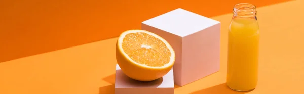 Suco fresco em garrafa de vidro perto de laranja metade e cubos brancos no fundo laranja, tiro panorâmico — Fotografia de Stock