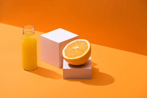 Frischer Saft in Glasflasche in der Nähe von Orangenhälfte und weißen Würfeln auf orangefarbenem Hintergrund — Stockfoto