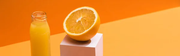 Suco fresco em garrafa de vidro perto da metade laranja e cubo branco no fundo laranja, tiro panorâmico — Fotografia de Stock