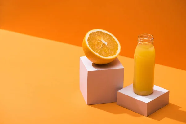 Zumo fresco en botella de vidrio cerca de la mitad naranja y cubos blancos sobre fondo naranja - foto de stock