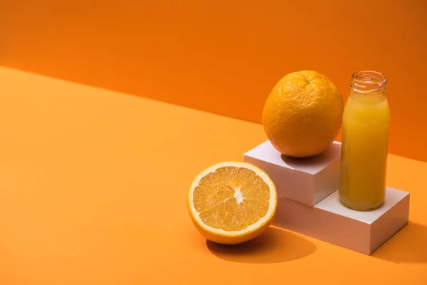 Fresh juice in glass bottle near oranges and white cubes on orange background — Stock Photo