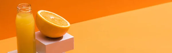 Zumo fresco en botella de vidrio cerca de la mitad naranja y cubos blancos sobre fondo naranja, plano panorámico - foto de stock