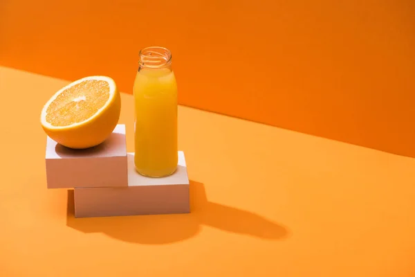 Suco fresco em garrafa de vidro perto da metade laranja e cubos brancos no fundo laranja — Fotografia de Stock