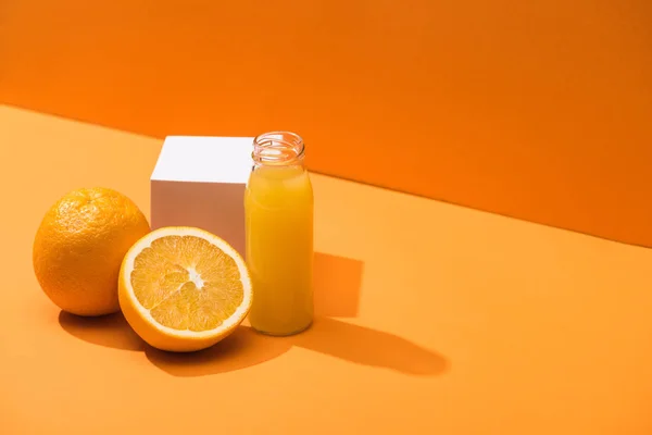 Zumo fresco en botella de vidrio cerca de naranjas y cubo blanco sobre fondo naranja - foto de stock