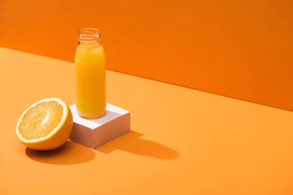 Jus frais en bouteille de verre près de la moitié orange et cube blanc sur fond orange — Photo de stock