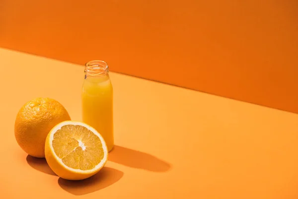 Suco fresco em garrafa de vidro perto de laranjas no fundo laranja — Fotografia de Stock