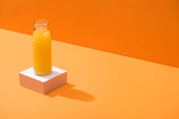 Suco fresco em garrafa de vidro no cubo branco no fundo laranja — Fotografia de Stock