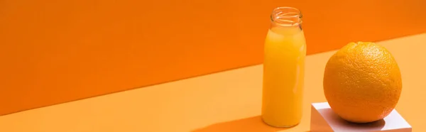 Zumo fresco en botella de vidrio cerca de cubo naranja y blanco sobre fondo naranja, plano panorámico - foto de stock