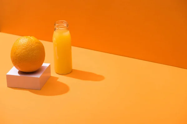 Jus frais en bouteille de verre près de l'orange entière et cube blanc sur fond orange — Photo de stock