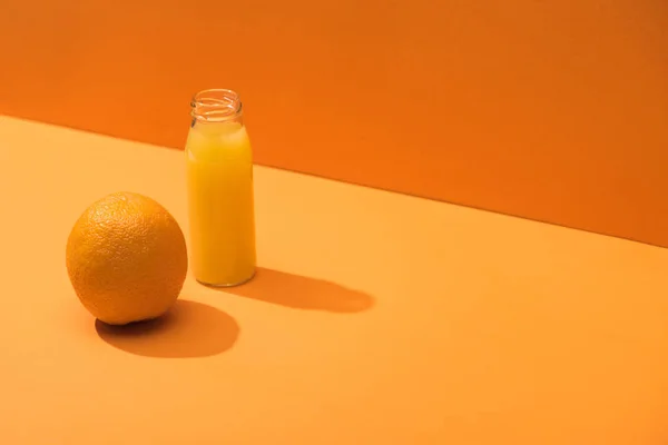 Jus frais en bouteille de verre près de l'orange entière sur fond orange — Photo de stock