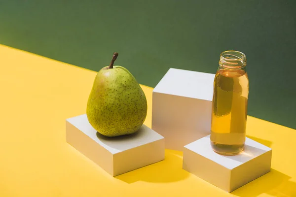 Frischer Saft in der Flasche in der Nähe von Birnen und weißen Würfeln auf grünem und gelbem Hintergrund — Stockfoto