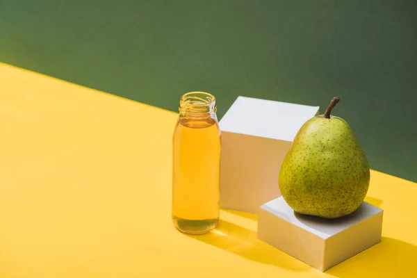 Suco fresco em garrafa perto de pêra e cubos brancos em fundo verde e amarelo — Fotografia de Stock