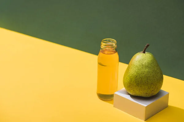 Fresh juice in bottle near pear and white cube on green and yellow background — Stock Photo