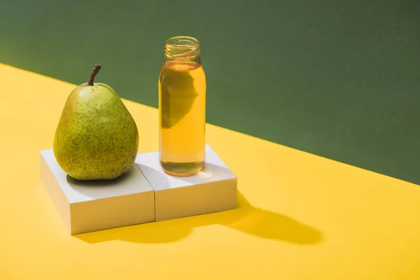 Frischer Saft in der Flasche in der Nähe von Birnen und weißen Würfeln auf grünem und gelbem Hintergrund — Stockfoto