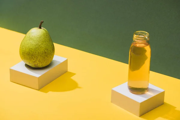 Frischer Saft in der Flasche in der Nähe von Birnen und weißen Würfeln auf grünem und gelbem Hintergrund — Stockfoto