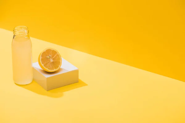 Fresh juice in bottle near lemon half and white cube on yellow background — Stock Photo