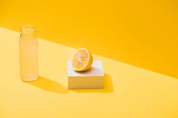 Jus frais en bouteille près de la moitié citron et cube blanc sur fond jaune — Photo de stock