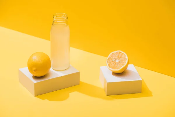 Suco fresco em garrafa perto de limões e cubos brancos no fundo amarelo — Fotografia de Stock