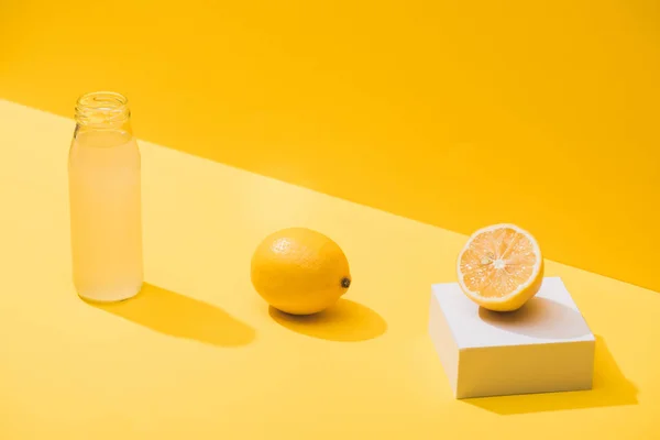 Свіжий сік у пляшці біля лимонів та білого кубика на жовтому фоні — стокове фото