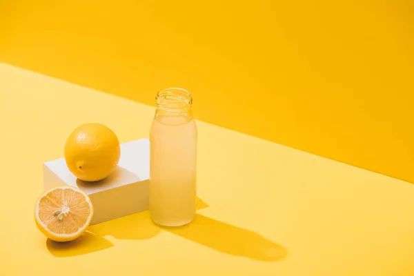 Свіжий сік у пляшці біля лимонів та білого кубика на жовтому фоні — стокове фото