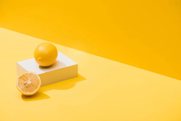 Fresh lemons and white cube on yellow background — Stock Photo