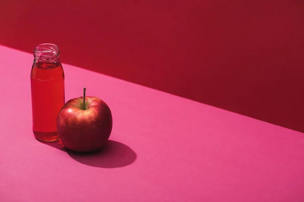 Fresh juice in bottle near apple on red and pink background — Stock Photo